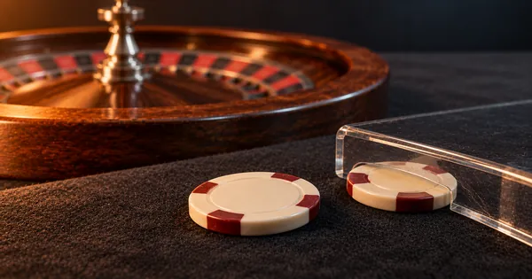 Two chips beside a roulette wheel, one under a clear holding edge